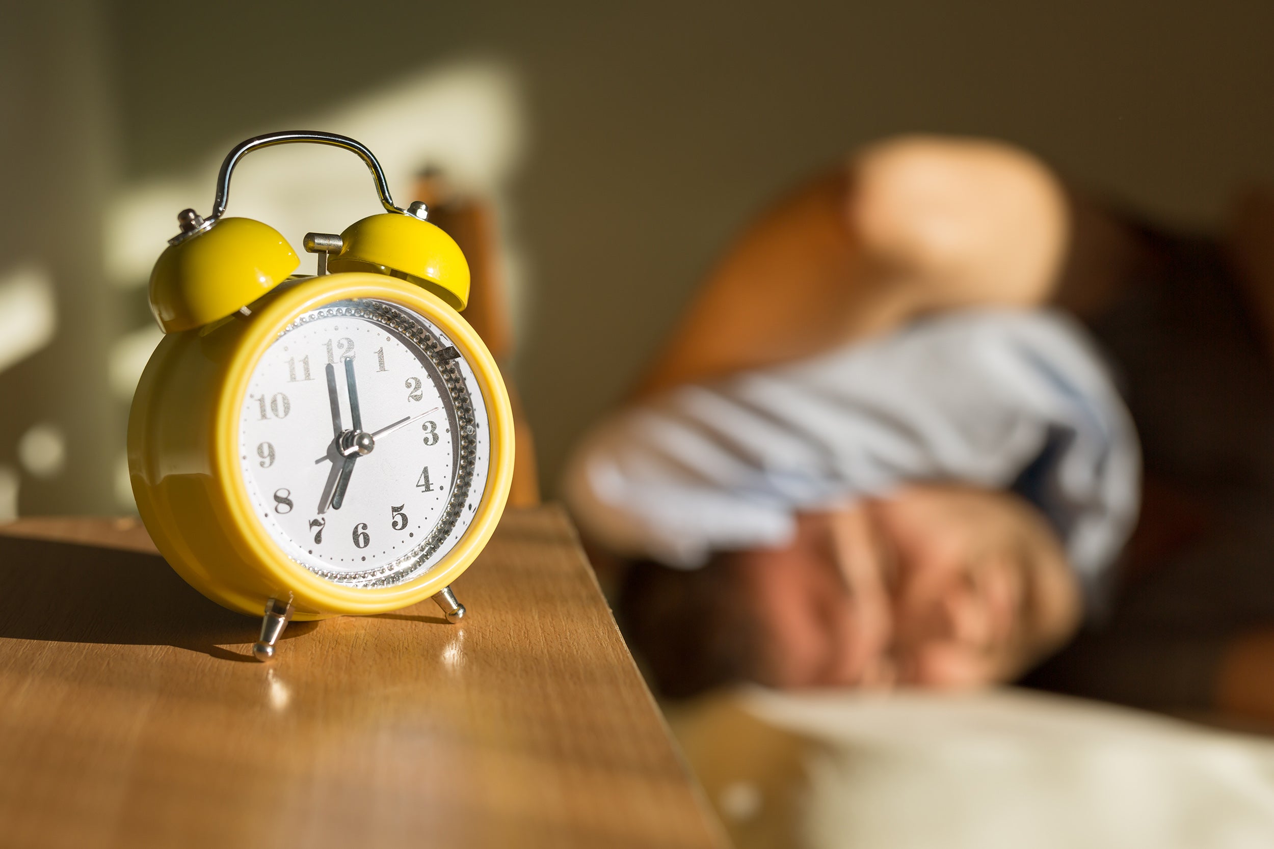 Person sleeping disturbed by alarm clock.